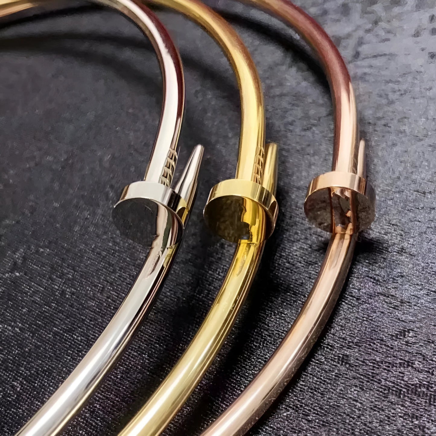 Close-up of three minimalist nail choker necklaces in silver, gold, and rose gold finishes, displayed on a sleek black surface, showcasing modern and elegant jewelry design.