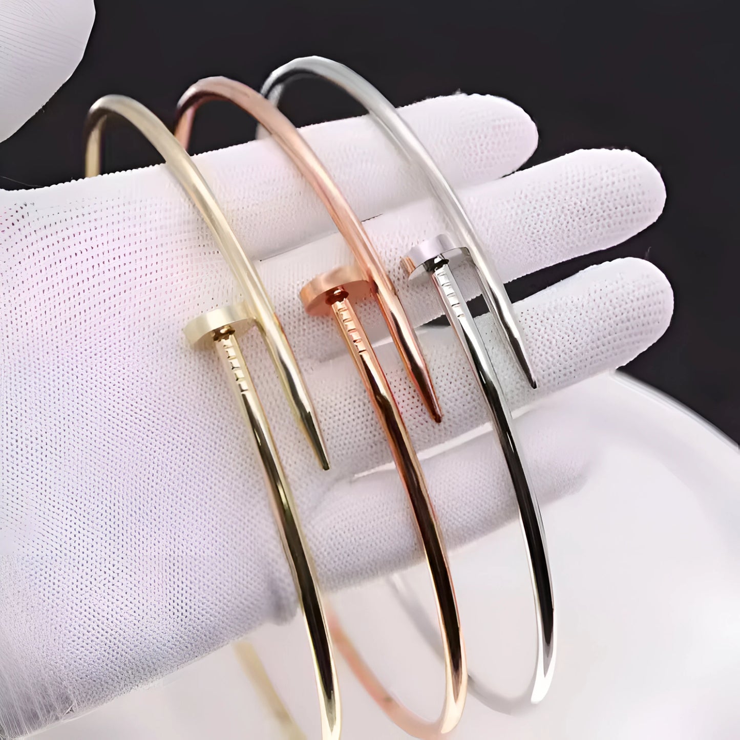 Luxury nail-shaped bracelets in gold, rose gold, and silver finishes are displayed on a white glove, highlighting modern minimalist jewelry design and premium craftsmanship.