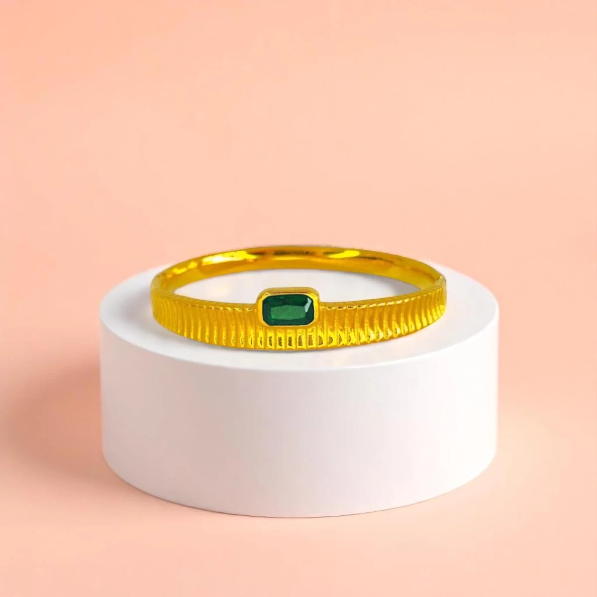 Bracelet displayed on a white pedestal against a soft peach background.