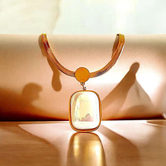 An 18K gold-plated stainless steel pendant necklace with an opal white stone centerpiece, displayed against a soft, warm background.