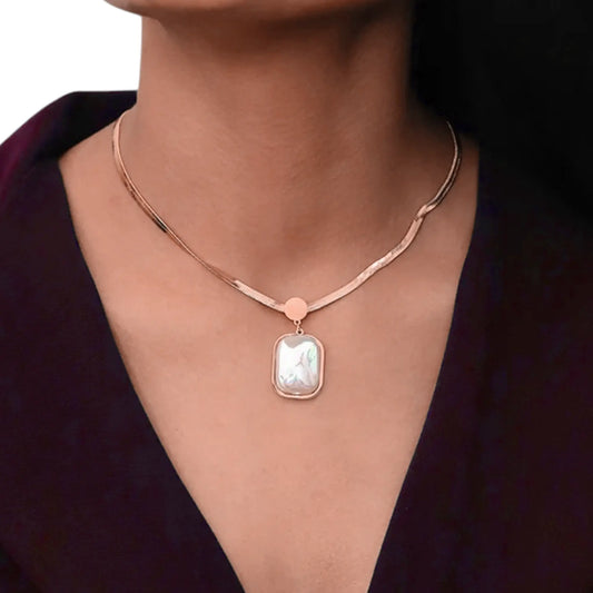Rose gold necklace with a pendant on a person wearing a dark purple top.
