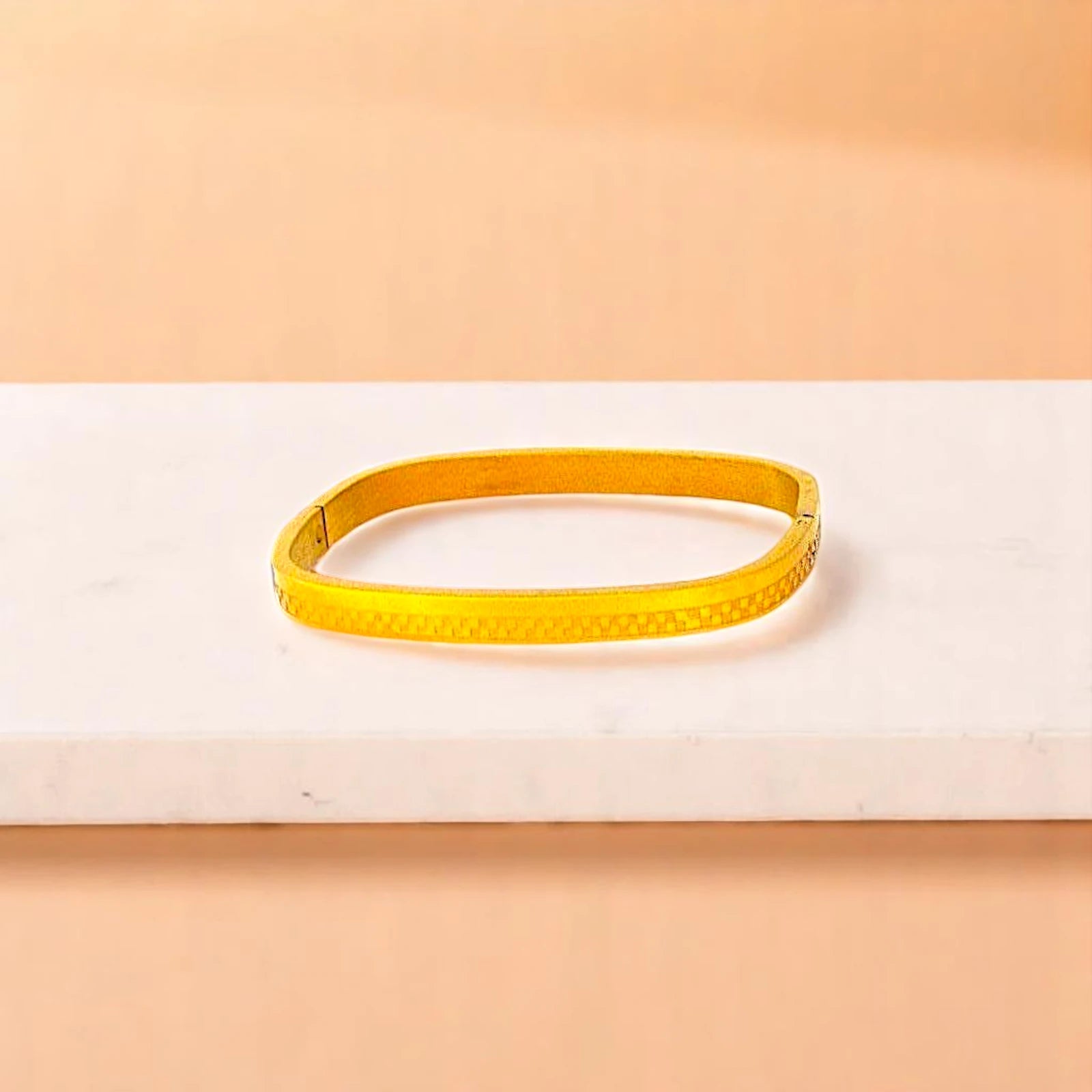 Bracelet on geometric prop with peach color gradient in the background.