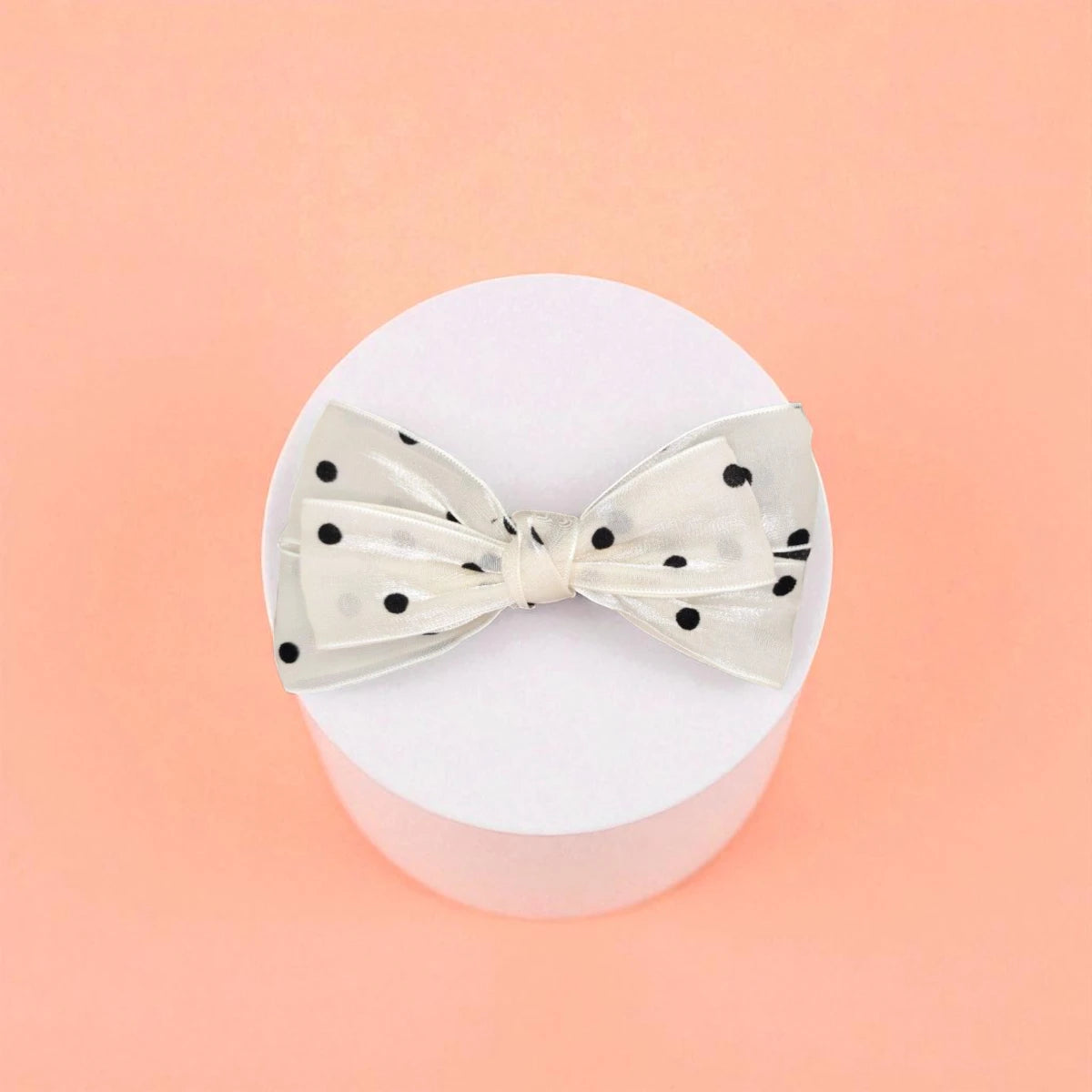 Bow with black polka dots on a white acrylic pedestal with a light background