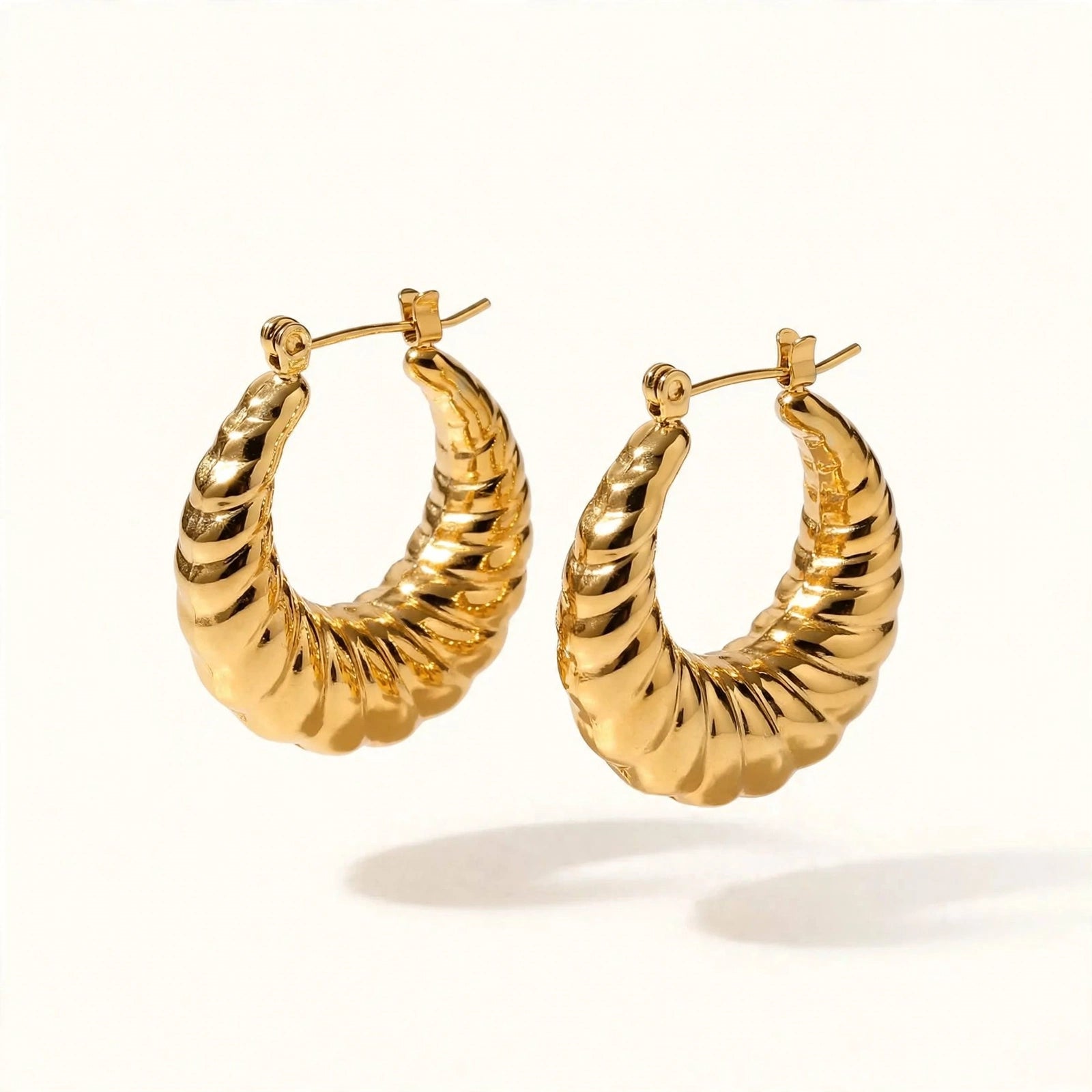 A pair of gold-toned twisted hoop earrings with a textured, ribbed surface, displayed on a clean off-white background.