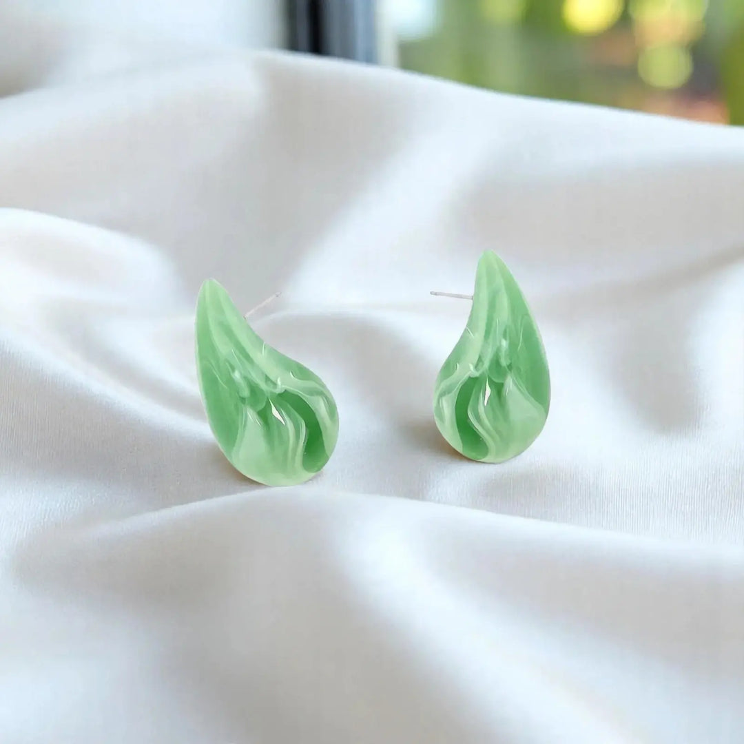 A pair of light green marbled teardrop-shaped earrings resting on draped white fabric.