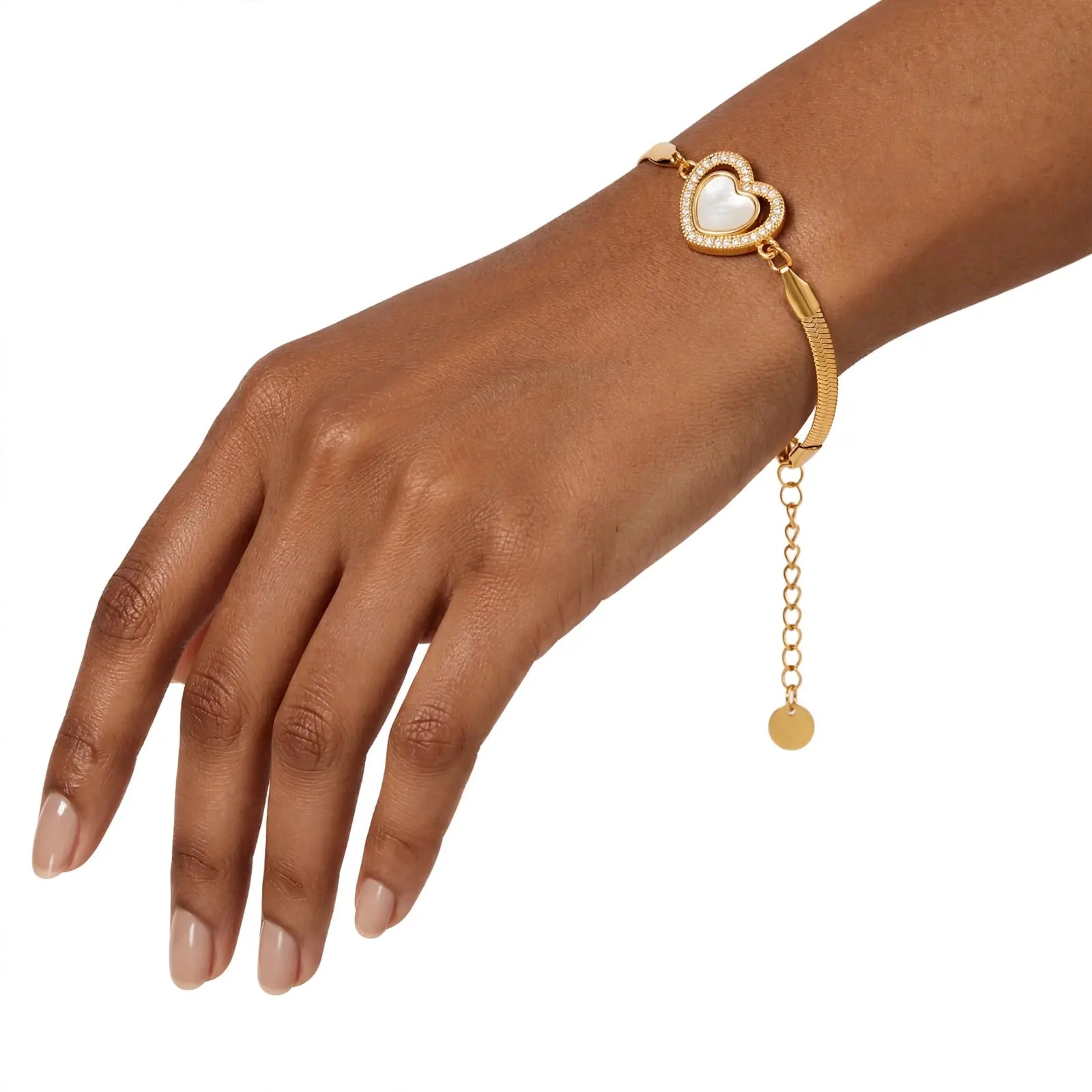 A gold heart-shaped charm bracelet with a textured band and a dangling chain, shown worn on a model's wrist against a plain white background.