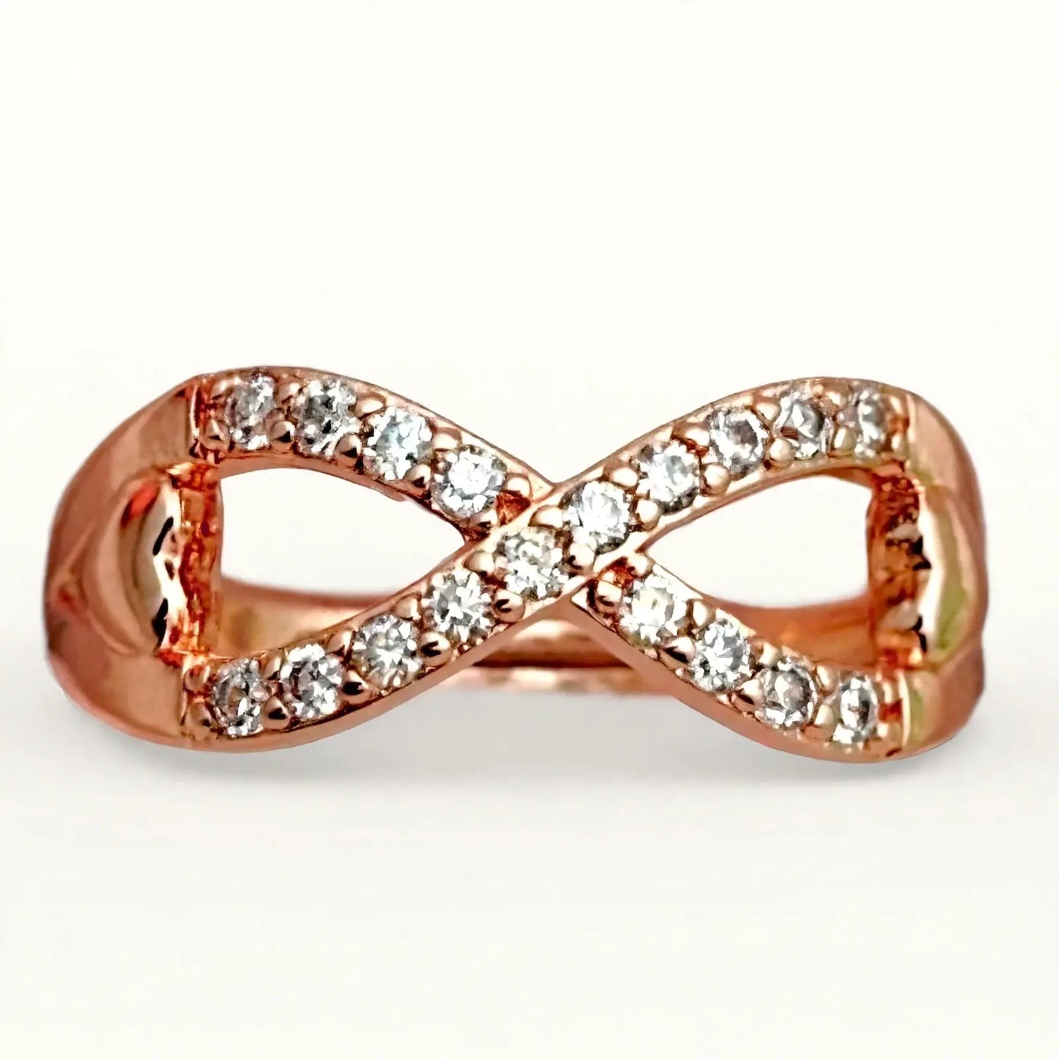 A rose gold infinity band ring set with clear cubic zirconia stones, shown on a clean white background.