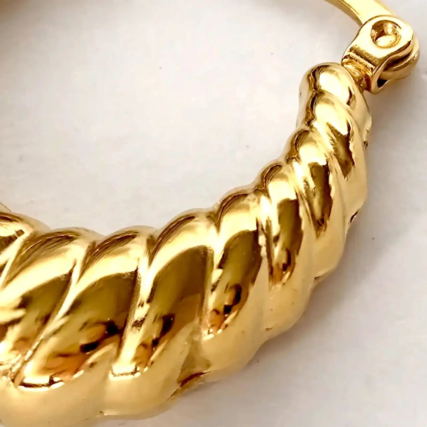 A close-up of a shiny gold rope-style bracelet or bangle on a plain light background.