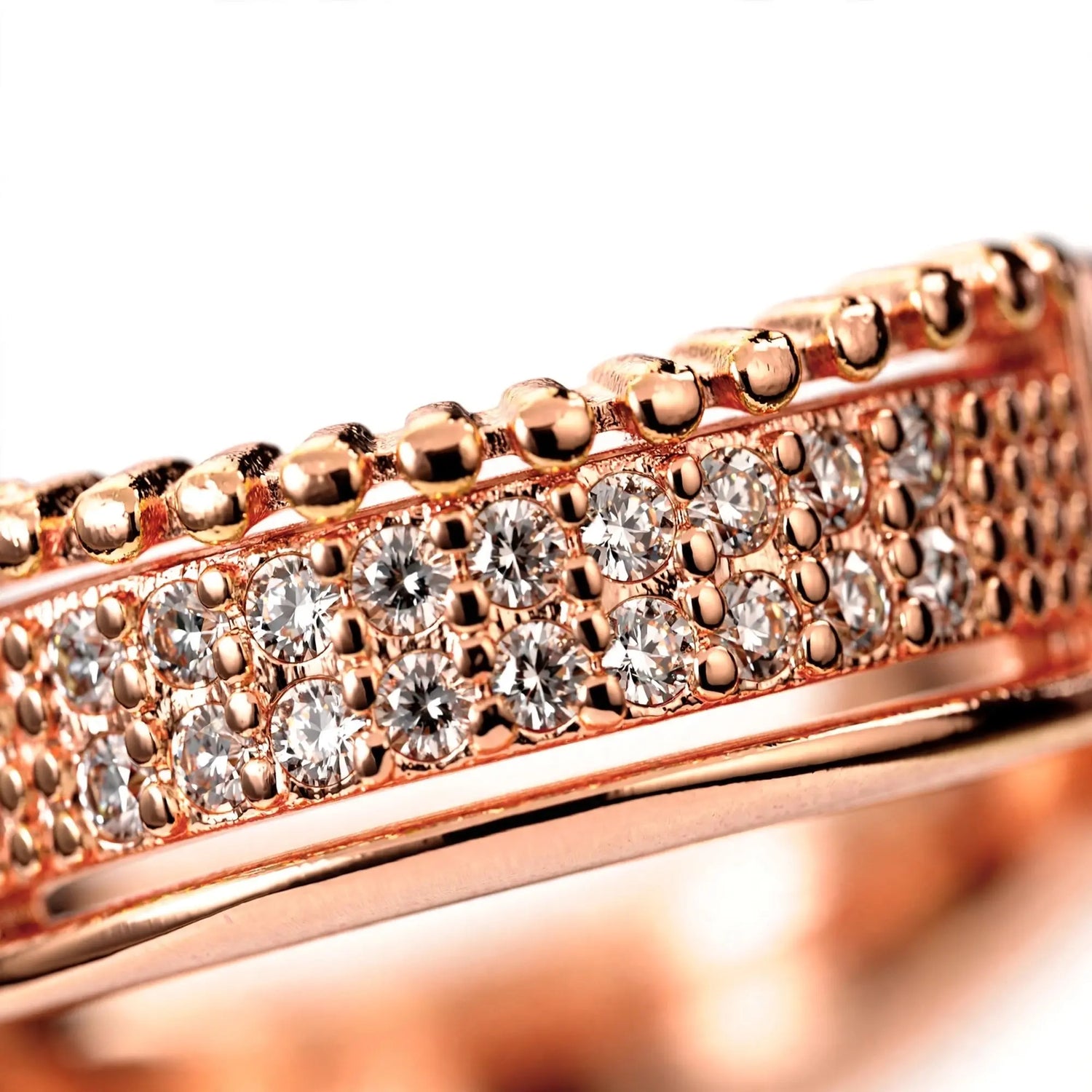 Close-up of a rose gold band ring featuring rows of clear pavé-set round diamonds and a raised beaded row along the top edge, set against a bright white background.