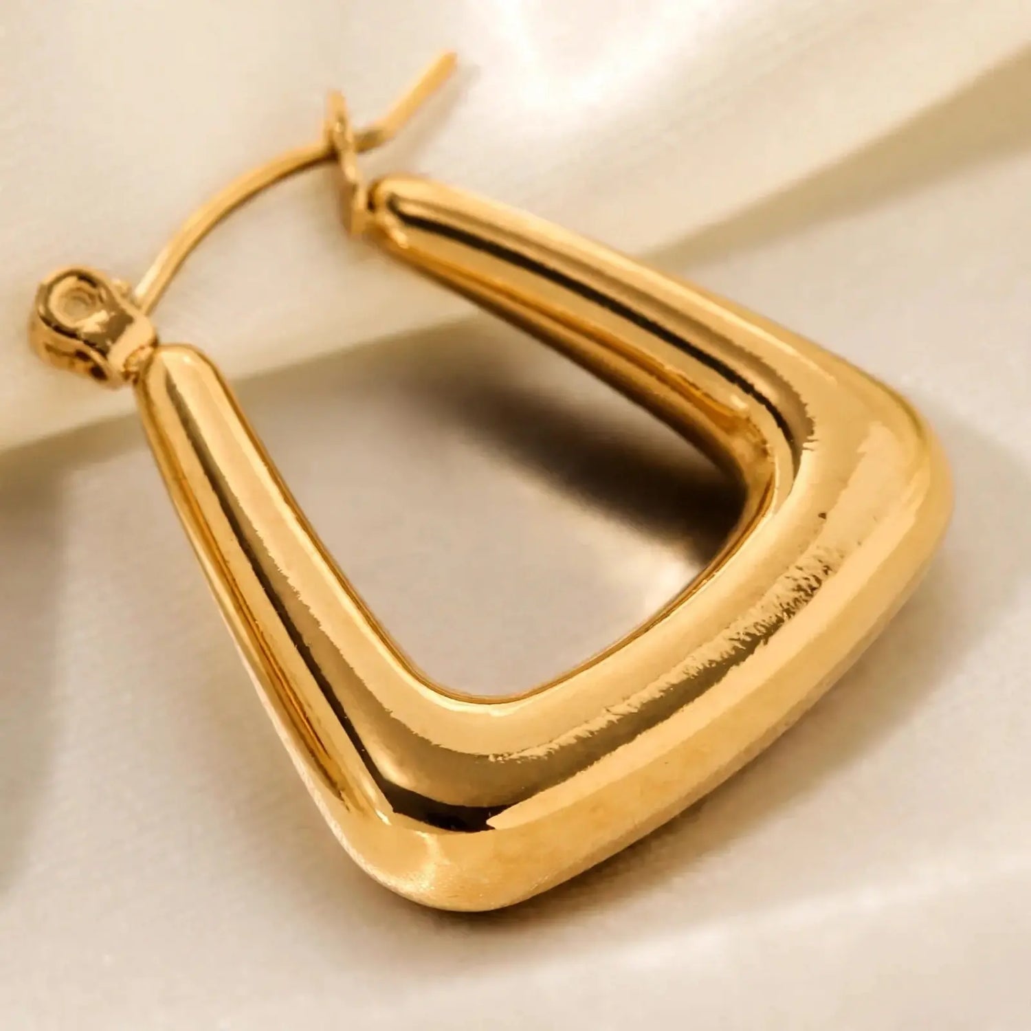 A single gold-toned hoop earring with a thick, rounded triangular open-frame design, photographed close-up on a light neutral background.