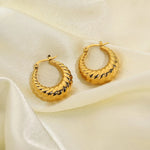 A pair of gold-toned twisted hoop earrings with black lightning-bolt accents, displayed on draped cream satin fabric.