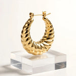 A gold hoop earring with a twisted, rope-like textured design, displayed on a clear acrylic block against a clean white background.