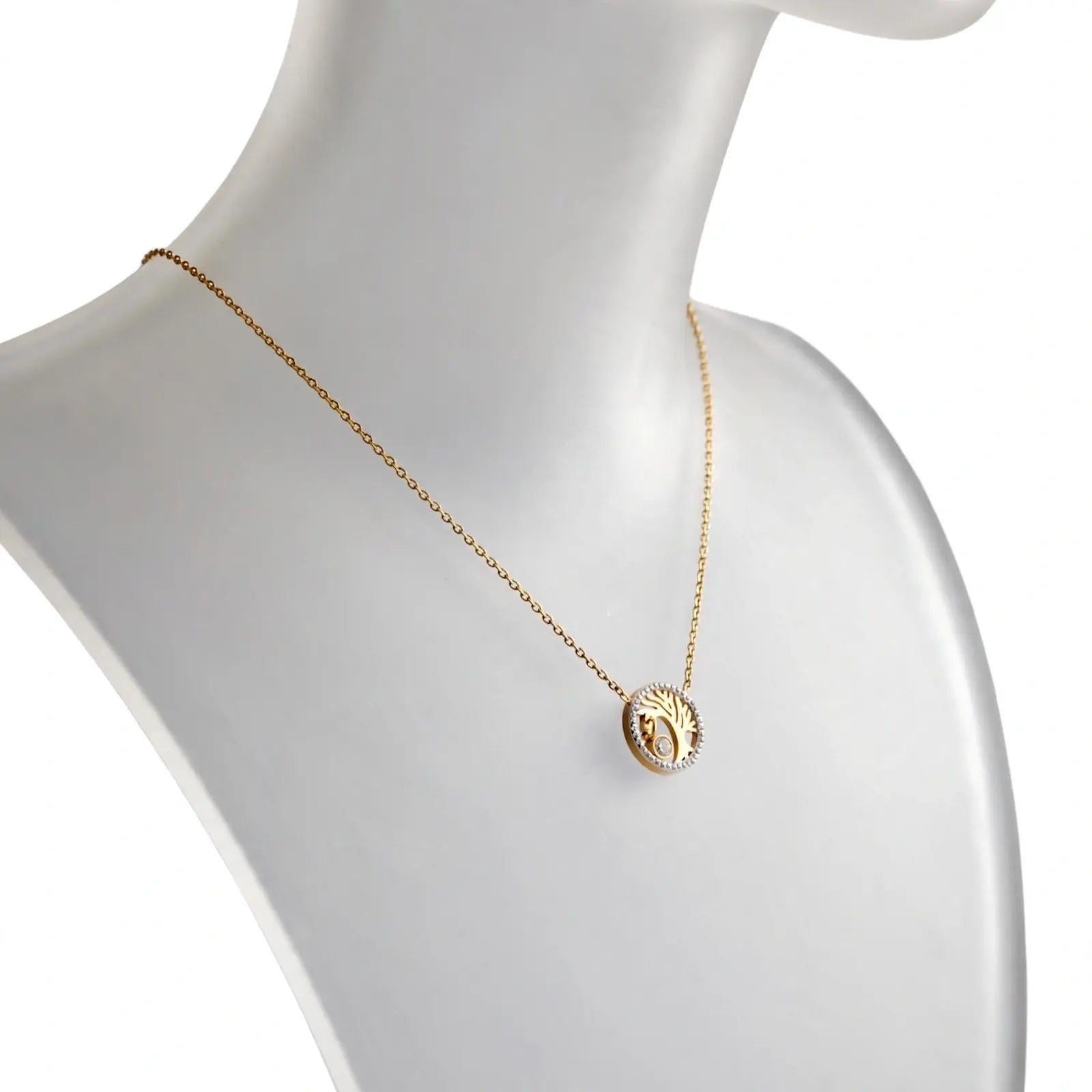 A delicate gold chain necklace with a circular pendant featuring a raised religious figure, displayed on a white mannequin bust against a clean white background.
