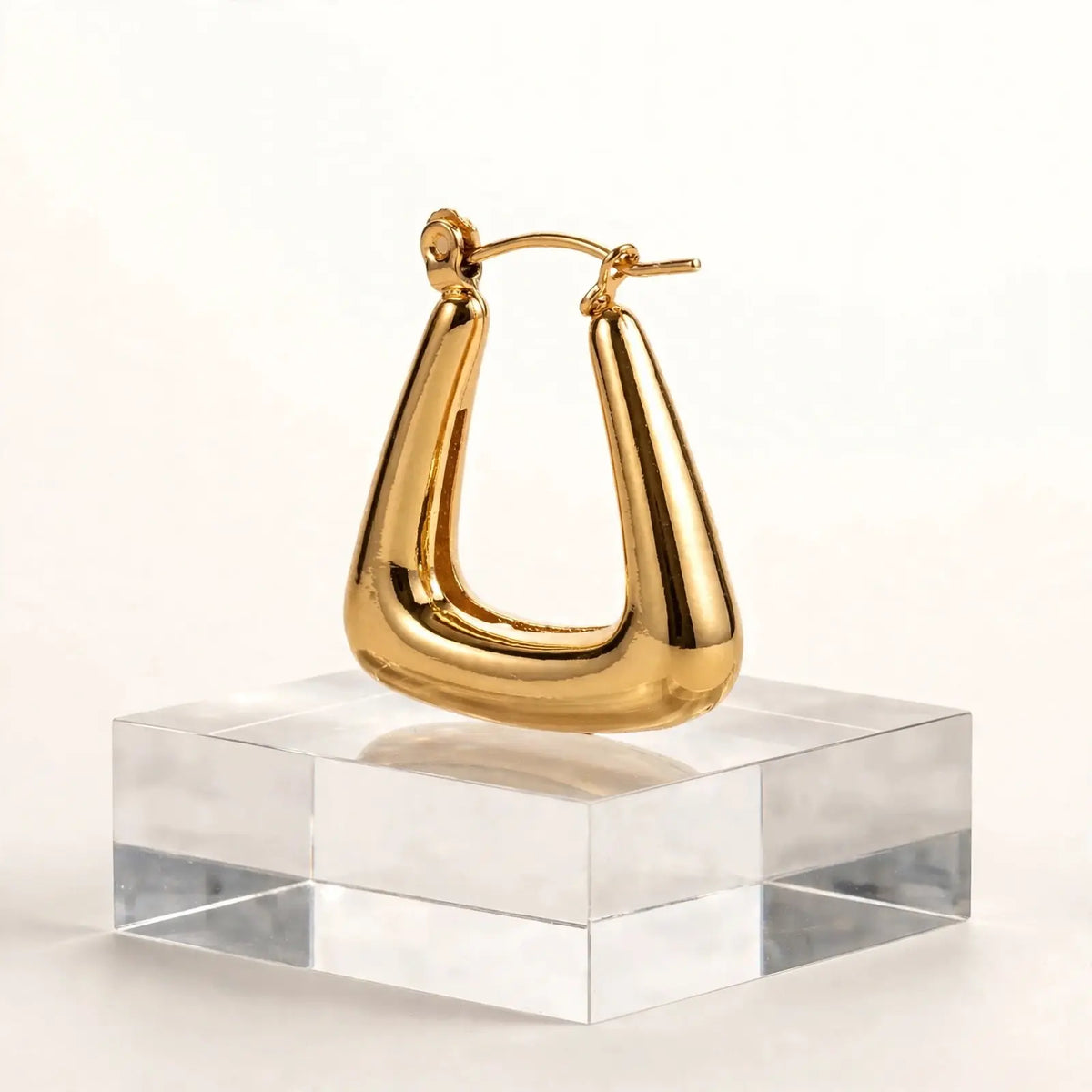 A single polished gold huggie hoop earring displayed on a clear acrylic block against a clean white background.