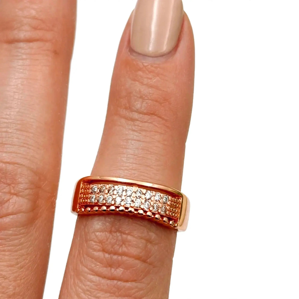 A rose gold ring with pavé-set clear stones, shown worn on a finger with a neutral manicure against a plain white background.