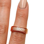 A rose gold ring with pavé-set clear stones, shown worn on a finger with a neutral manicure against a plain white background.