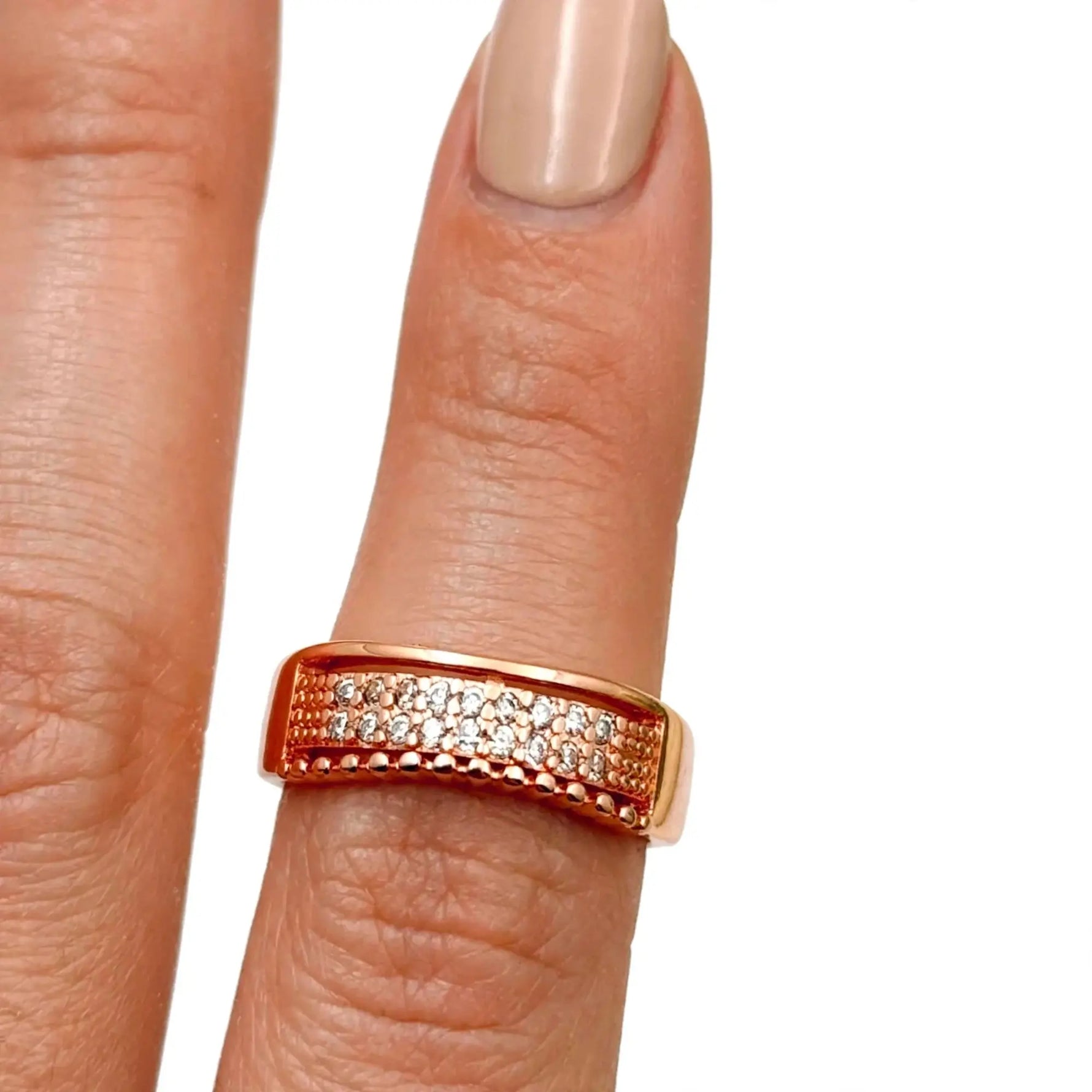 A rose gold ring with pavé-set clear stones, shown worn on a finger with a neutral manicure against a plain white background.