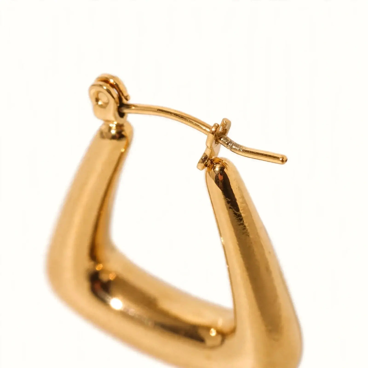 A close-up shot of a gold hoop earring with a unique curved, teardrop-like shape and a post with a butterfly back, set against a plain white background.