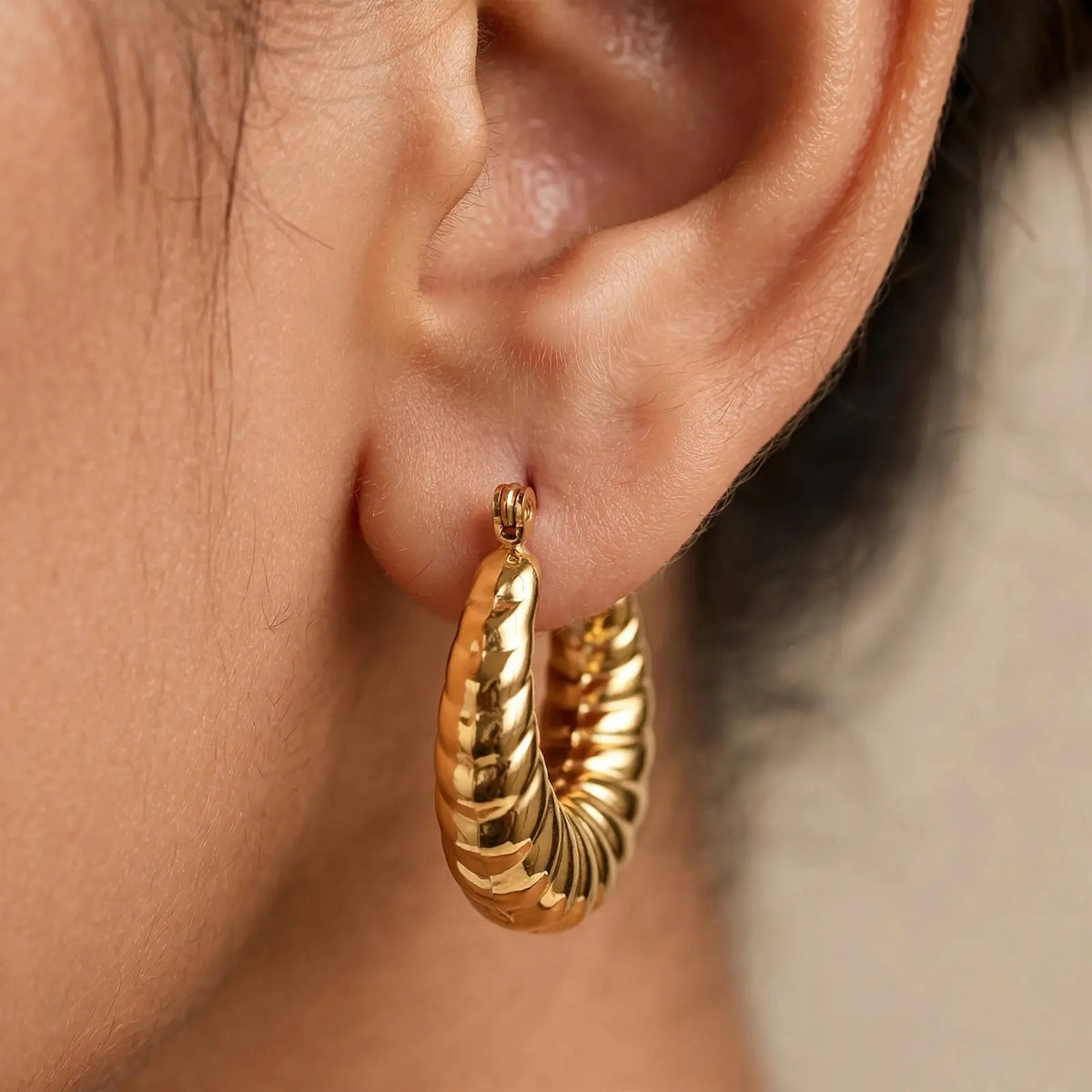 A close-up of a person's ear wearing a textured gold hoop earring.