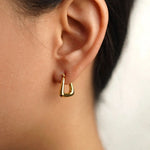 A close-up of a person's ear wearing a small polished gold hoop earring.