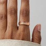 A close-up of a person's hand wearing a rose gold ring with a textured band and a row of small clear stones.