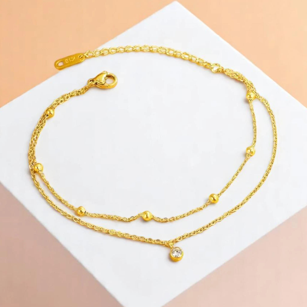 Anklet on a geometric prop with a peach-colored gradient in the background.