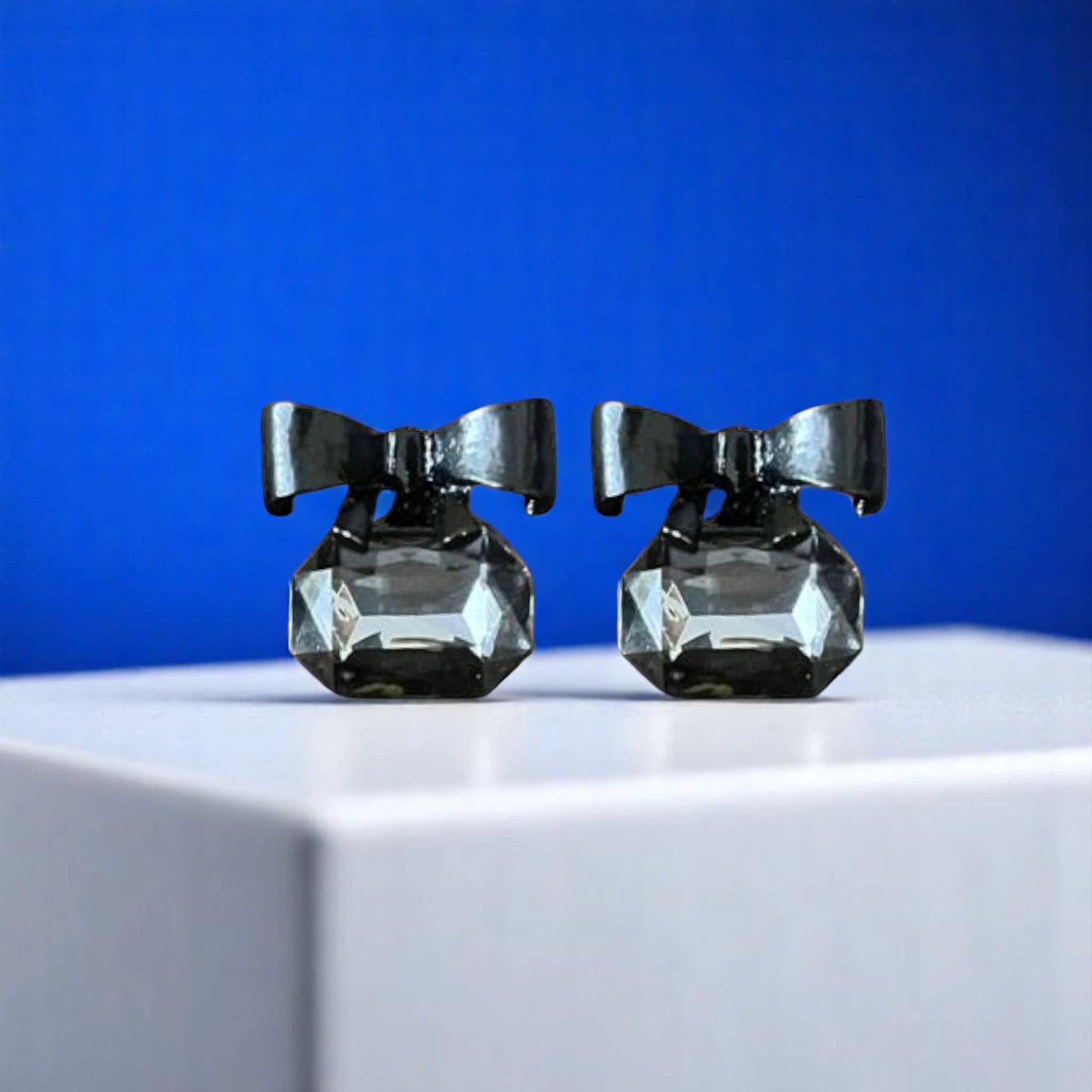 Elegant black hair accessories featuring diamond-like gems and bows, displayed on a white pedestal against a vibrant blue background.
