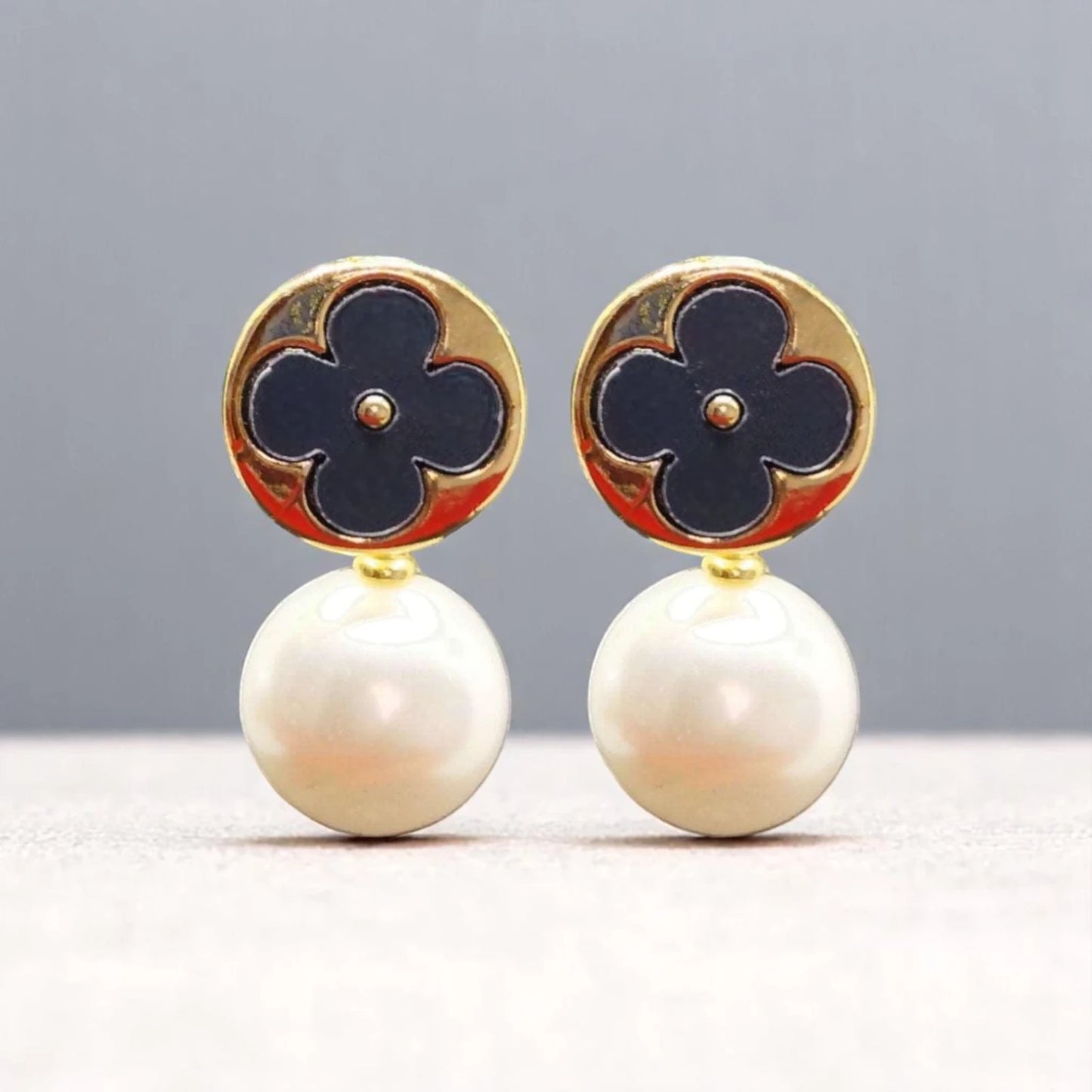 Elegant earrings featuring a gold circular top with a navy flower design, complemented by lustrous white pearl drops.