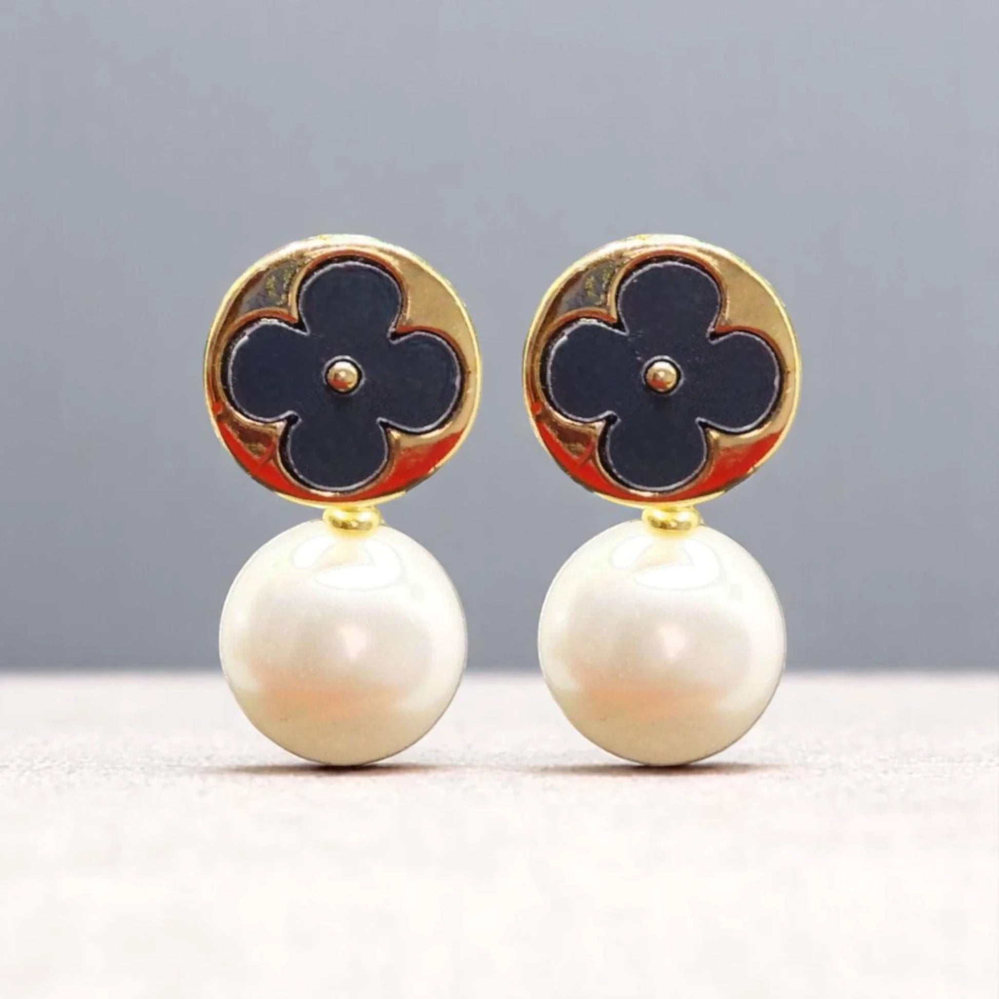 Elegant earrings featuring a gold circular top with a navy flower design, complemented by lustrous white pearl drops.