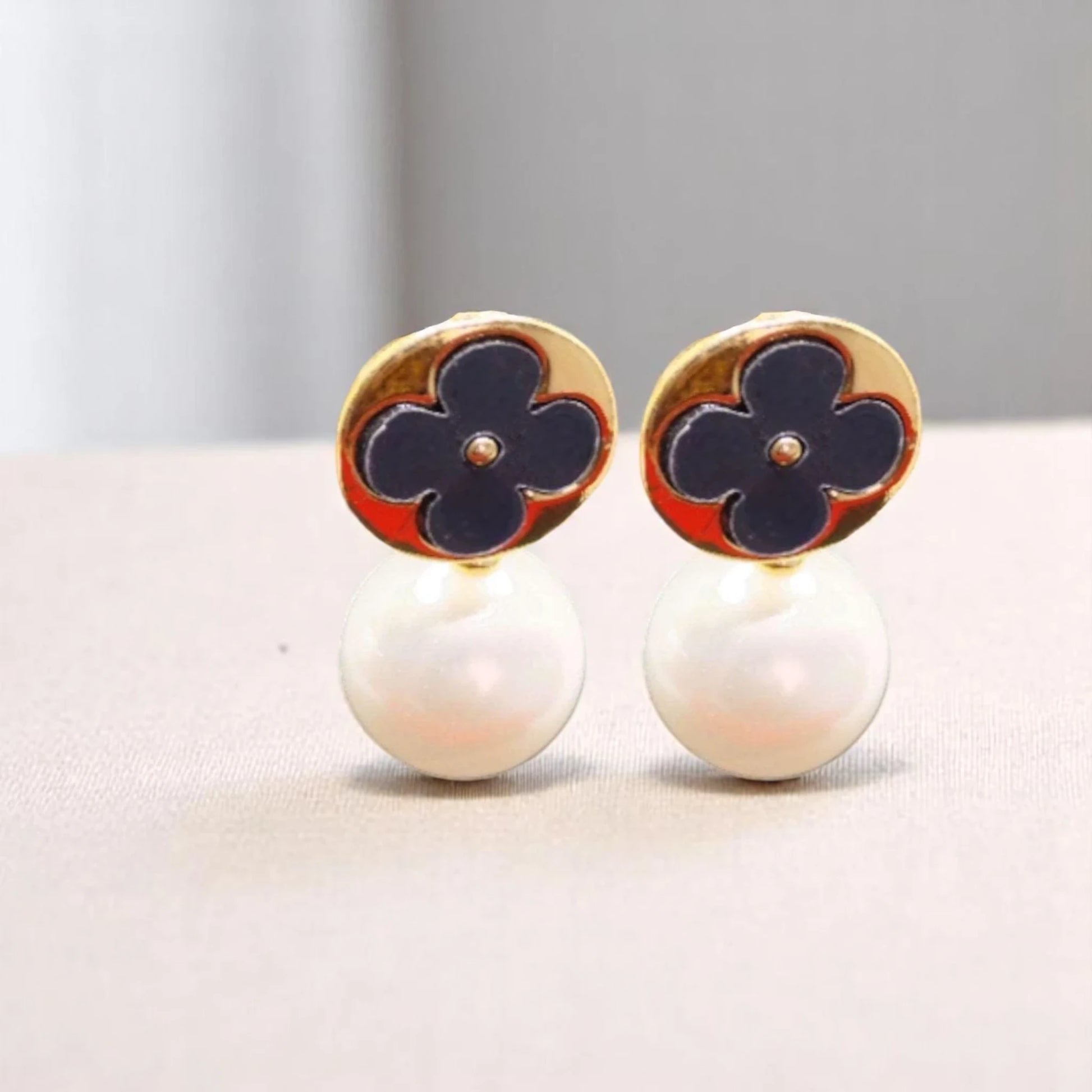 Elegant gold earrings featuring navy blue floral designs atop white pearl drops, combining classic and modern aesthetics.