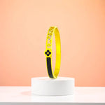 Bracelet displayed on a white pedestal against a soft peach background.