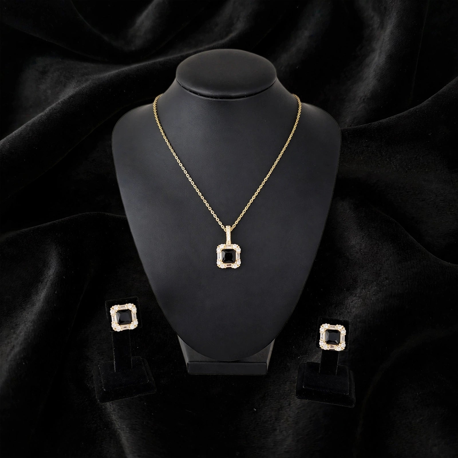 Gold square pendant necklace and matching stud earrings displayed on a black jewelry bust against a black velvet background.