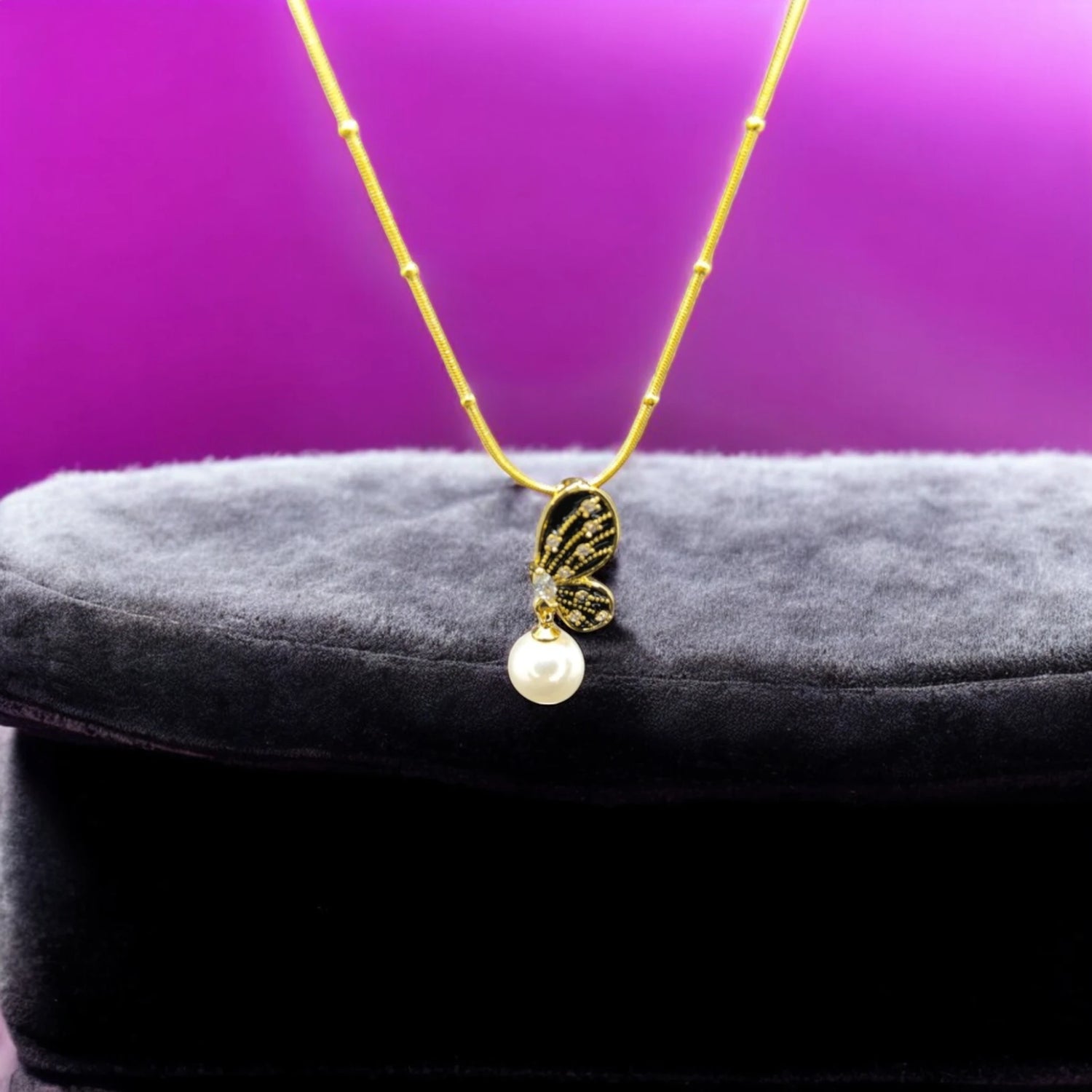 Butterfly Necklace with Pearl Drop on soft fabric box with a purple background.