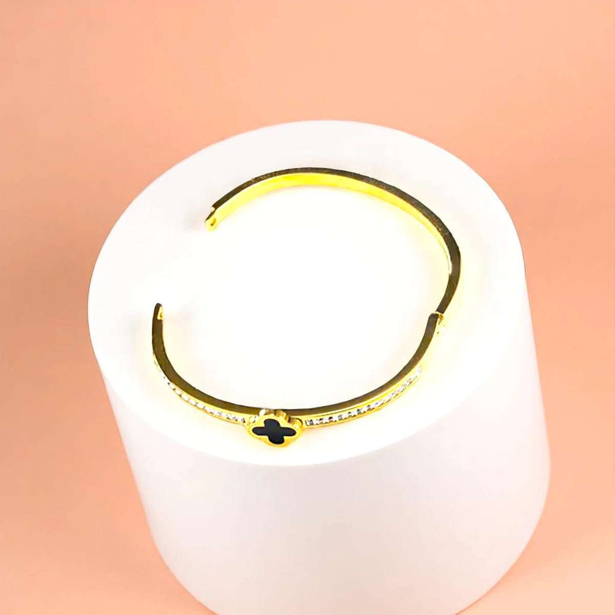 Bracelet displayed on a white pedestal against a soft peach background.