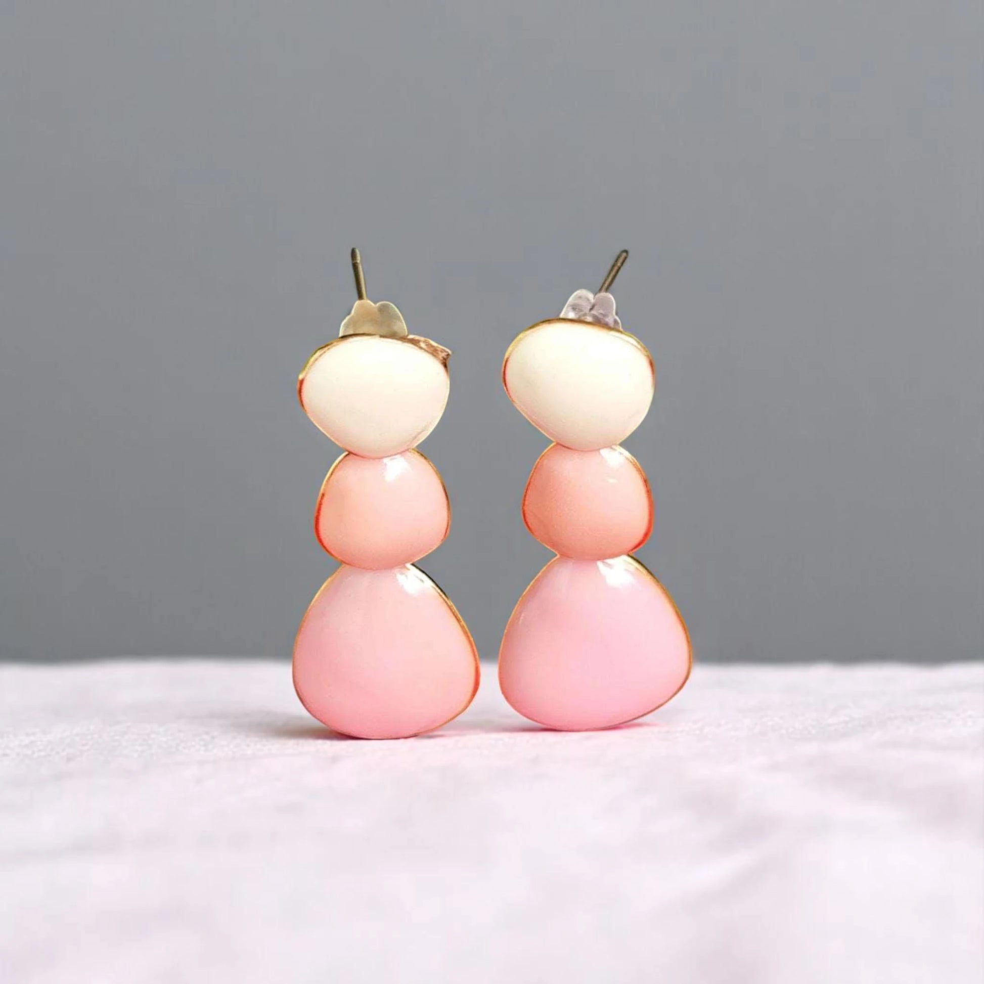 Colorful, modern dangle earrings featuring stacked pastel pink and cream shapes, set against a soft, neutral background.