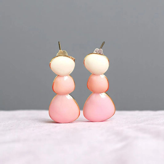 Colorful, modern dangle earrings featuring stacked pastel pink and cream shapes, set against a soft, neutral background.