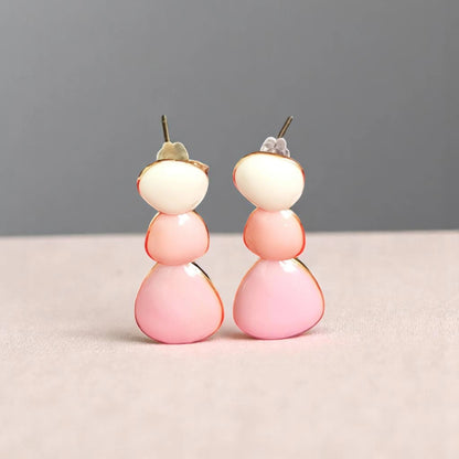 A pair of stylish earrings featuring three stacked, rounded beads in soft pink and cream hues, outlined in gold.