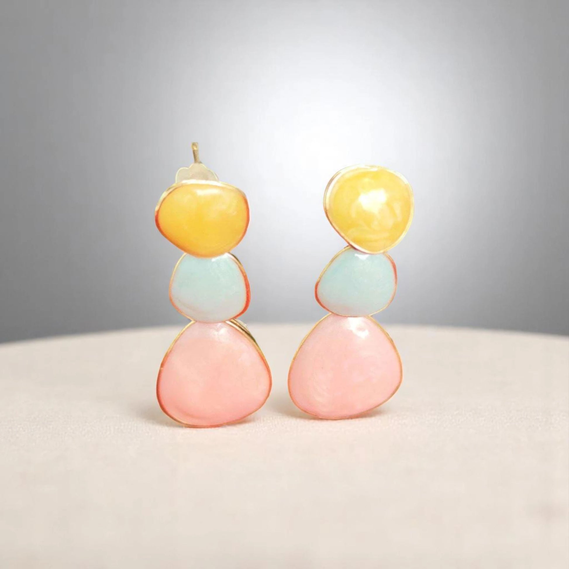 Colorful modern earrings featuring stacked gemstones in yellow, blue, and pink, set in delicate gold edges on a soft surface.