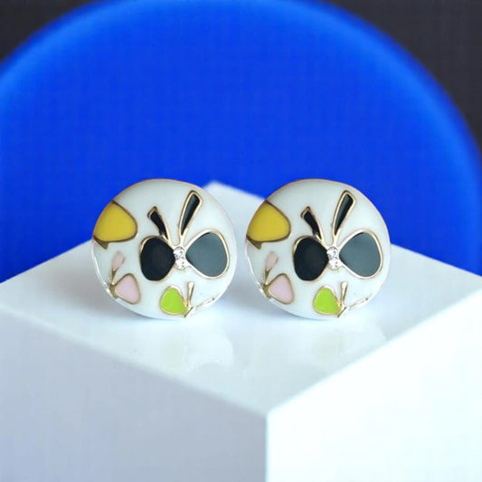 Colorful round earrings with floral designs in green, yellow, pink, and black, displayed on a white pedestal against a blue background.