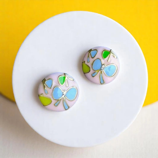 Colorful round earrings with delicate designs showcased on a white ceramic plate against a vibrant yellow background.