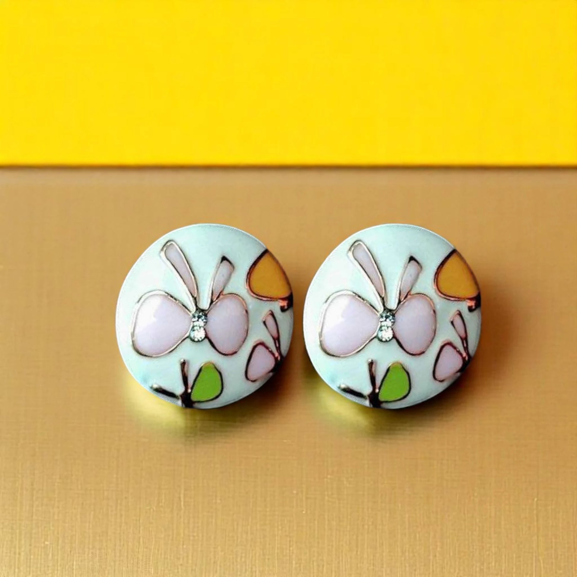 Round earrings featuring pastel-colored butterflies and floral designs, set against a gold background.