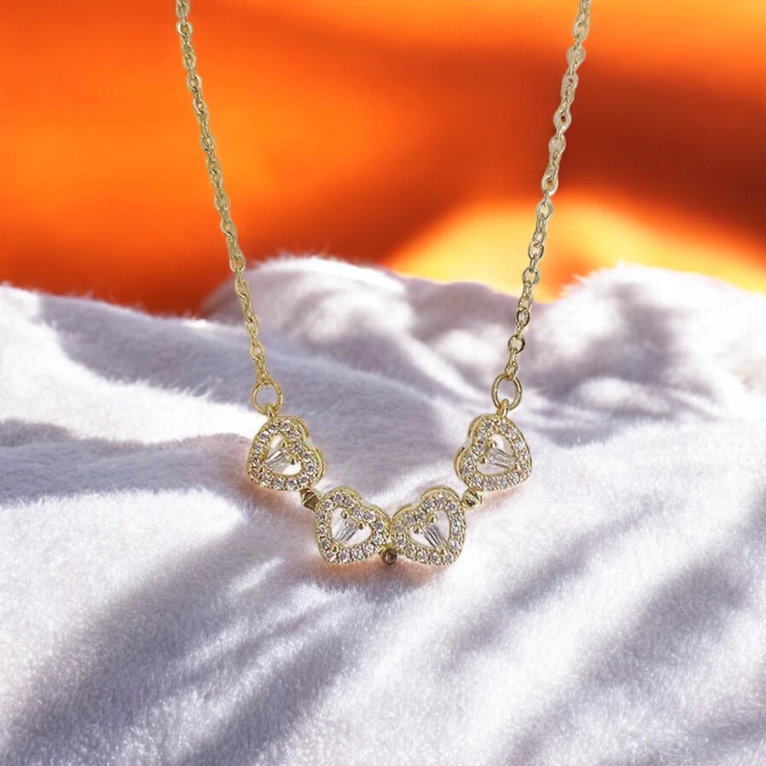 Gold heart necklace with sparkling details resting on soft white fabric, illuminated by a warm orange background.
