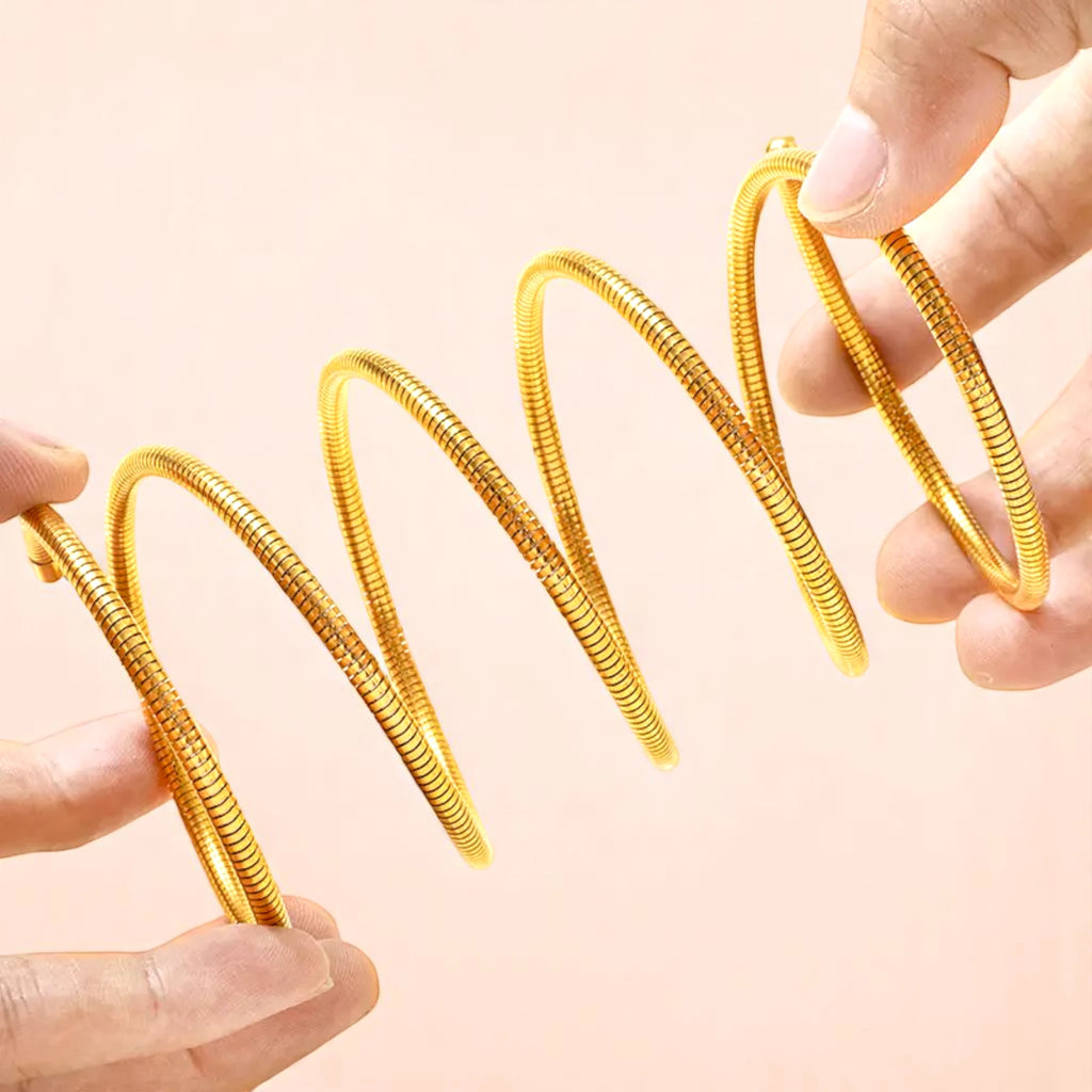 Two hands holding a swirling, shiny gold metal spring, showcasing its coiled design against a soft pink background.