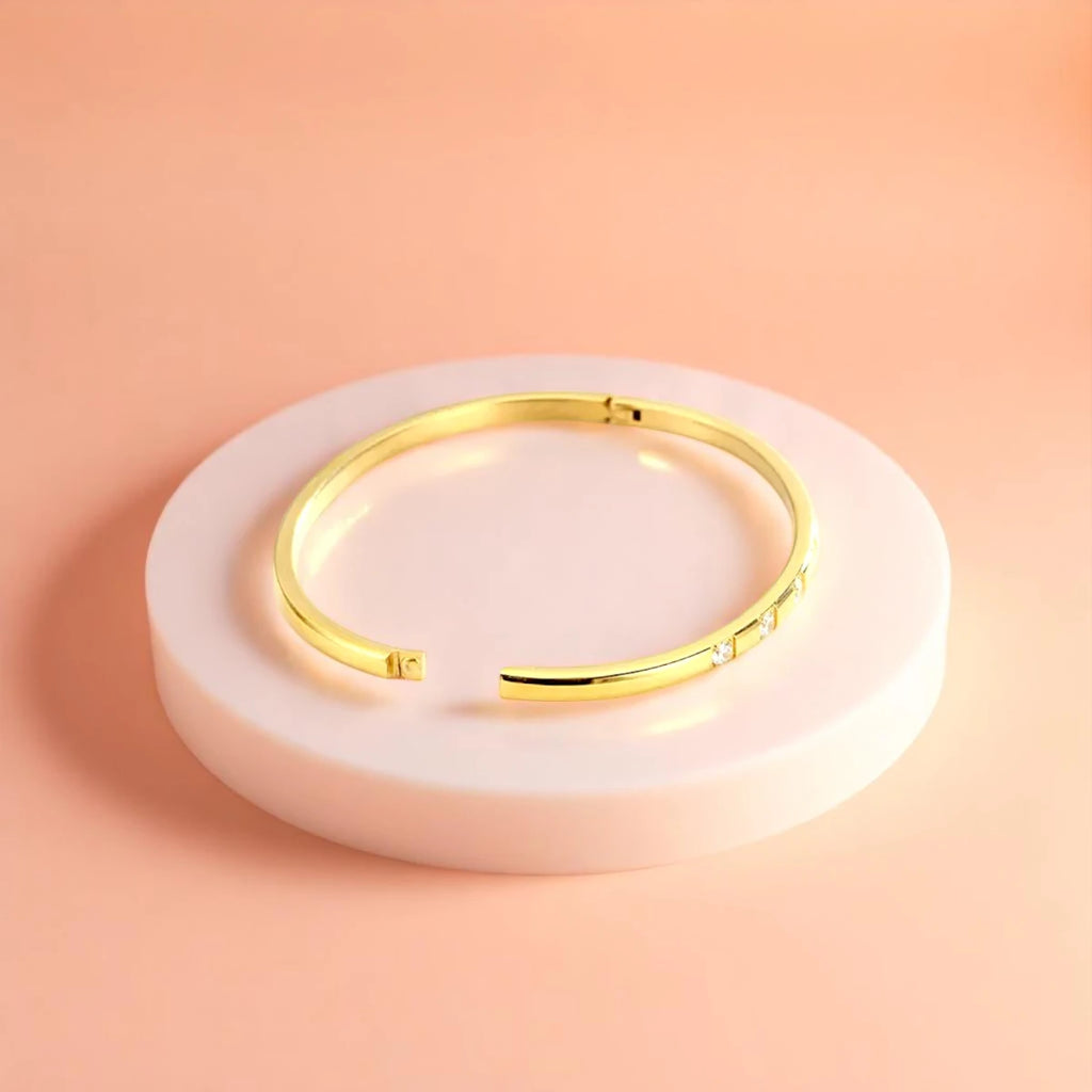 Bracelet displayed on a white pedestal against a soft peach background.