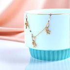 Bracelet rests on a light blue cup against a soft pink backdrop.