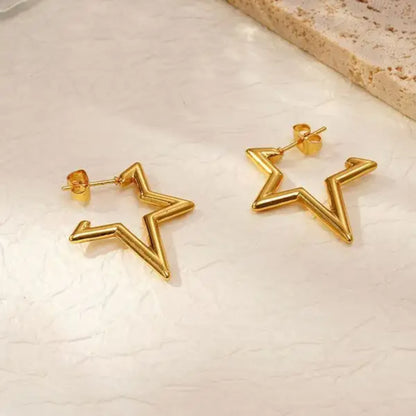 Gold star-shaped earrings with a sleek, angular design, resting on a textured surface.