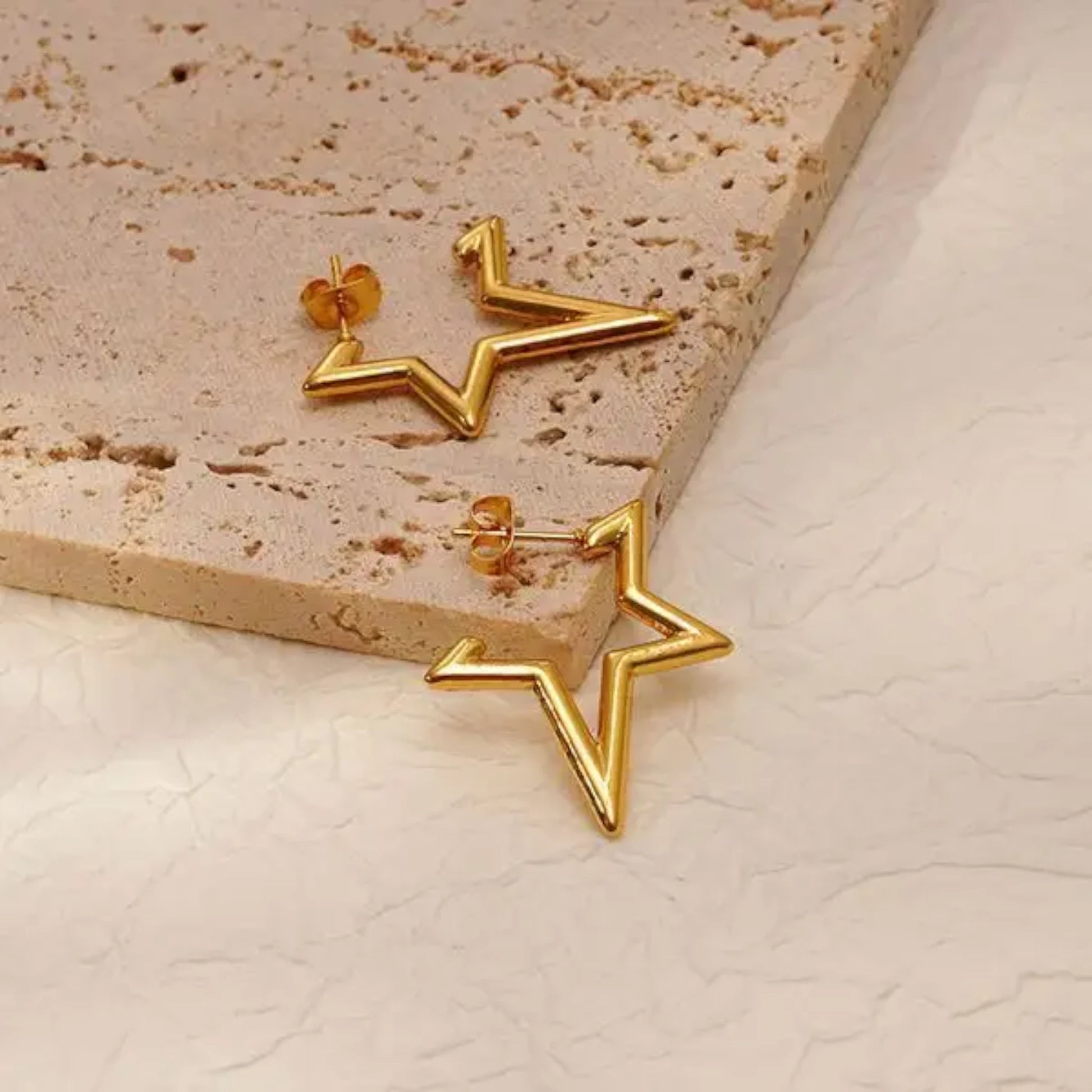 Gold star-shaped earrings resting on a textured beige surface, showcasing a modern and stylish design.