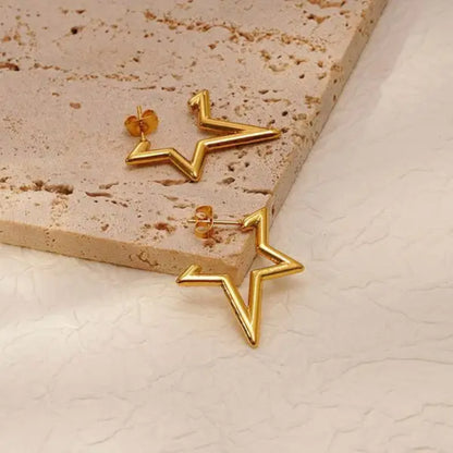 Gold star-shaped earrings resting on a textured beige surface, showcasing a modern and stylish design.