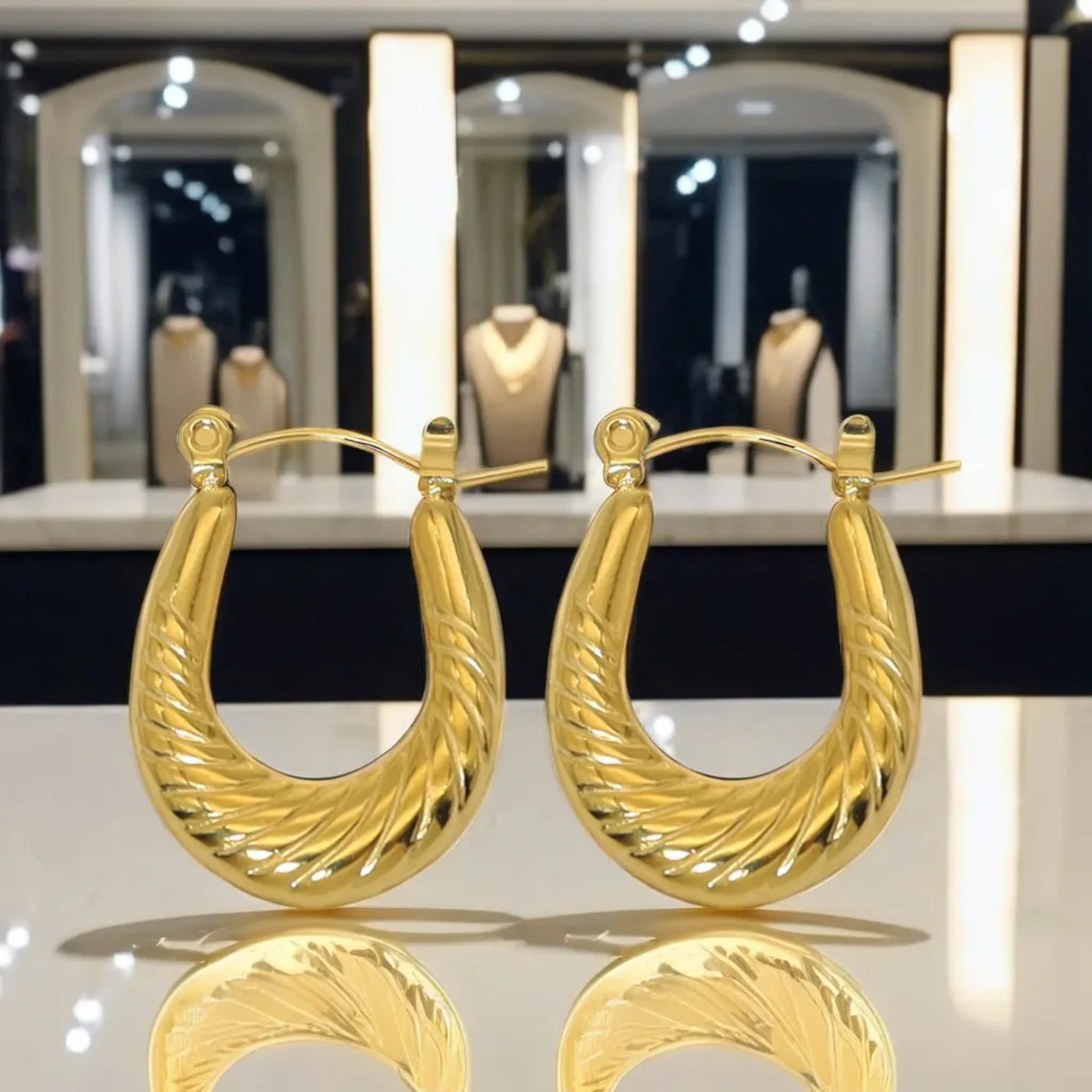 A pair of elegant gold hoop earrings with a twisted design displayed on a reflective surface in a jewelry store.
