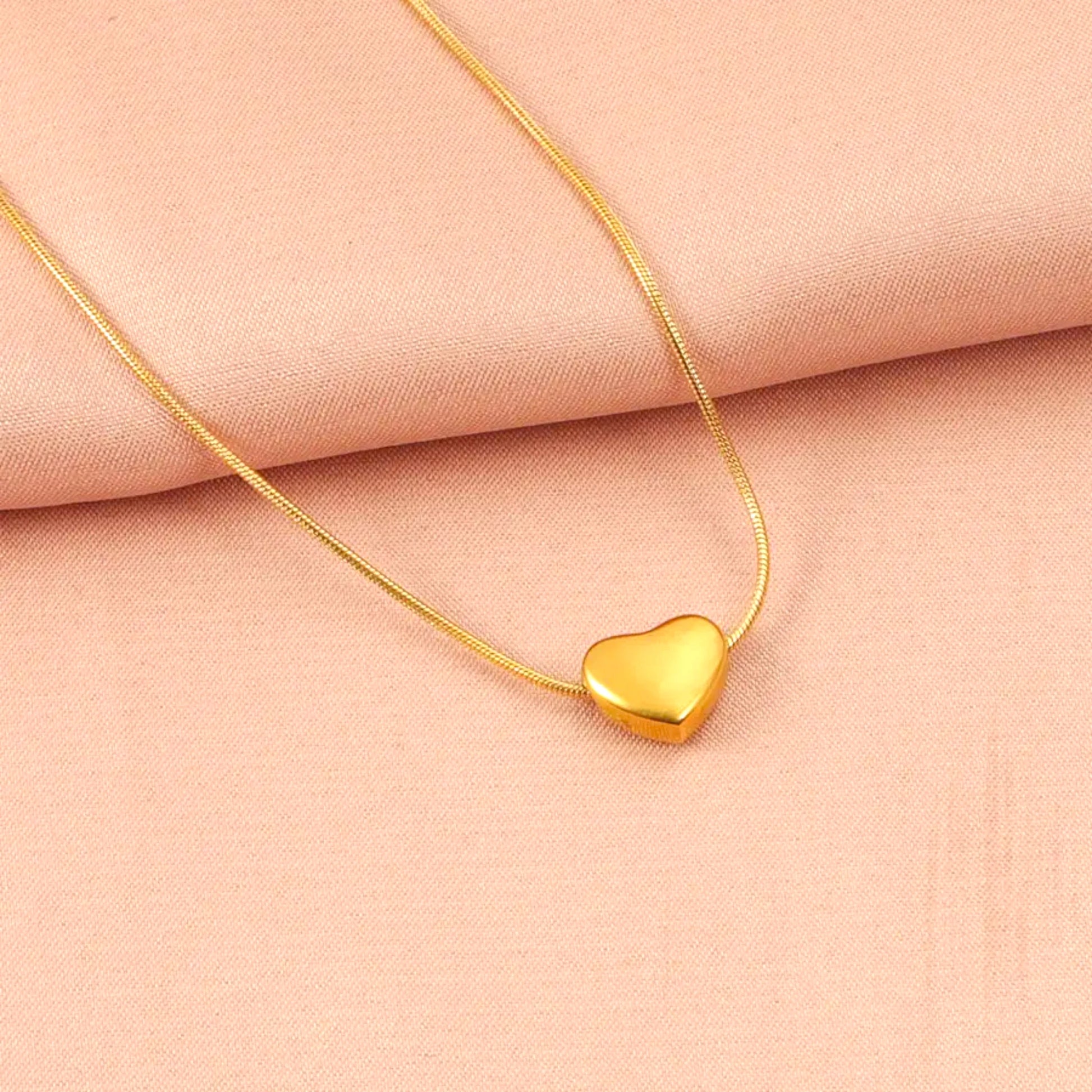 Gold heart pendant necklace resting on a soft peach fabric background.